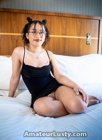Light-skin amateur model in a short black dress posing on a bed.